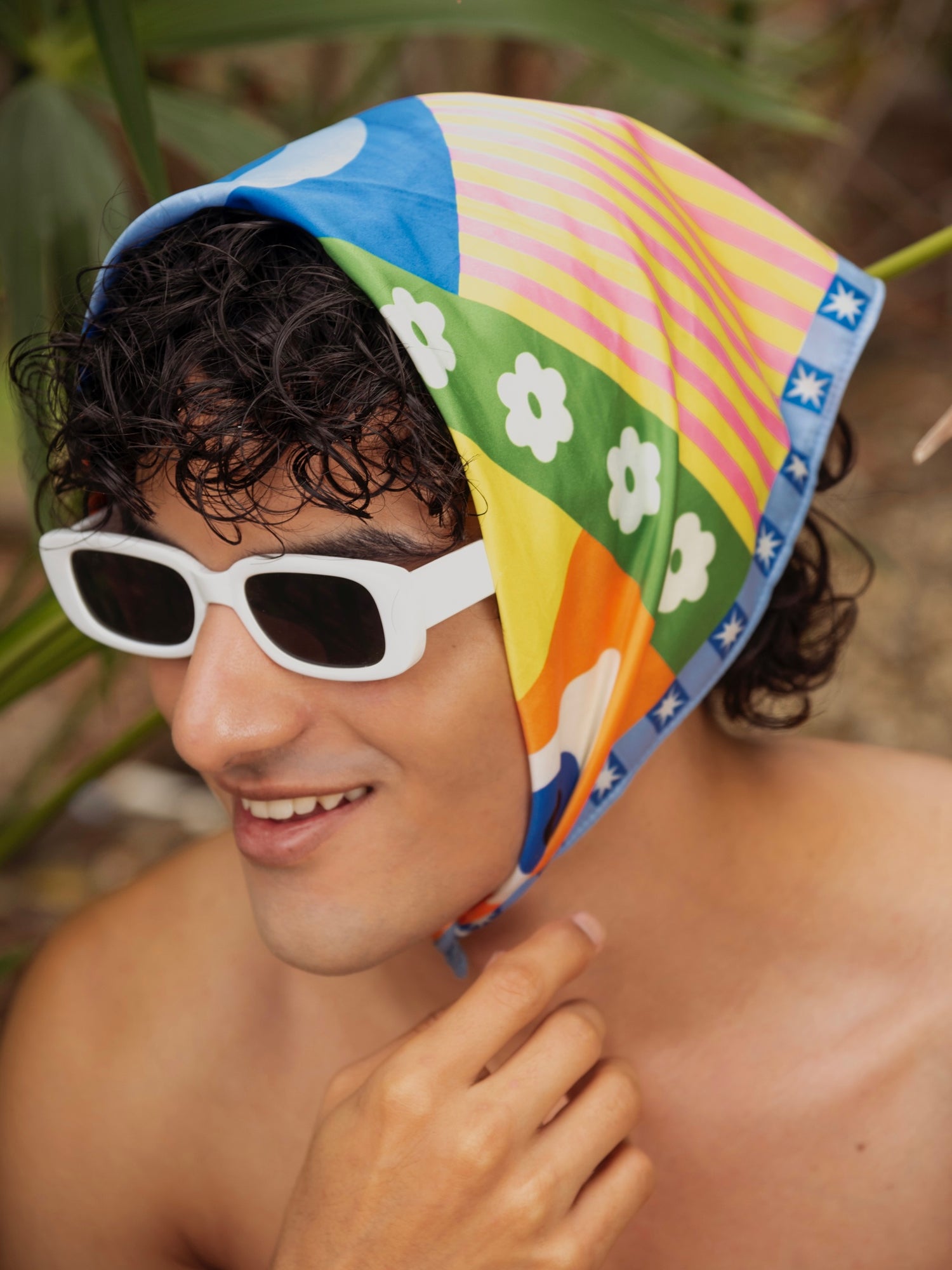 Person wearing a colorful headscarf with floral patterns and white sunglasses outdoors.
