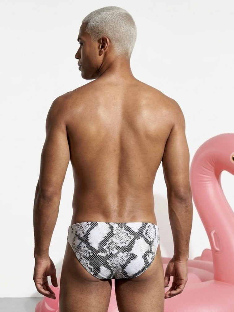 Man wearing snake print swim briefs with a pink flamingo pool float in the background