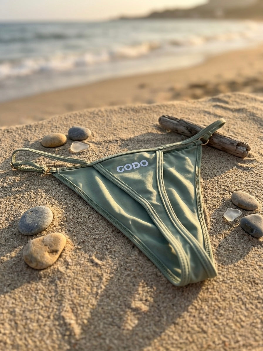 Green male thong with 'GODO' branding on a sandy beach.