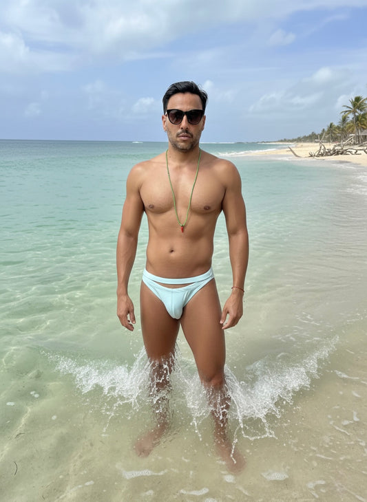 Man in light blue swim trunks standing in shallow water on a beach