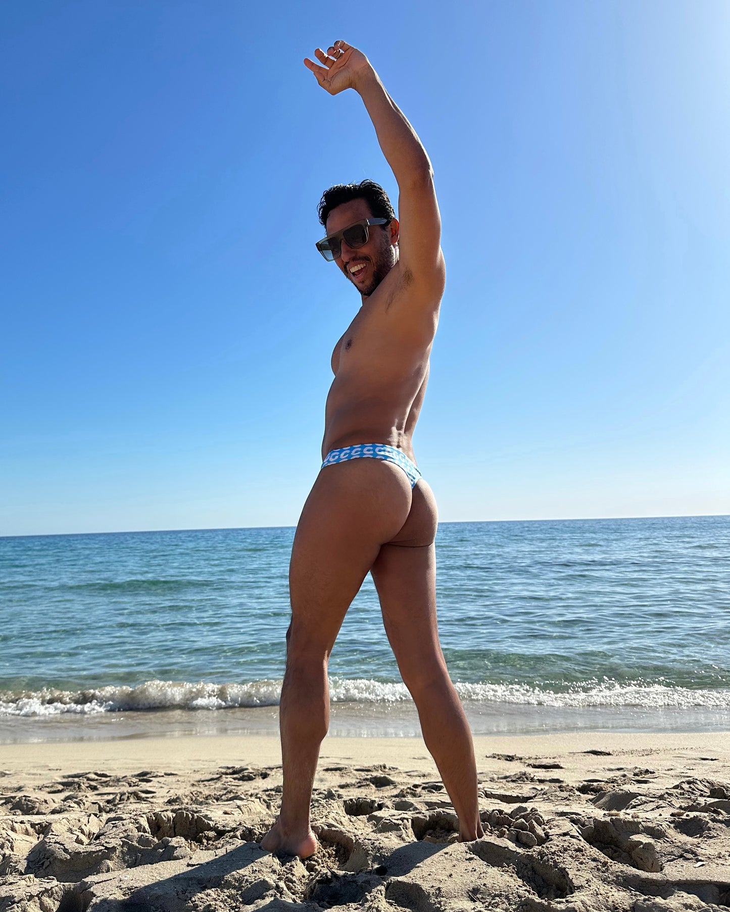 Man in thong on a beach with ocean and clear sky in the background