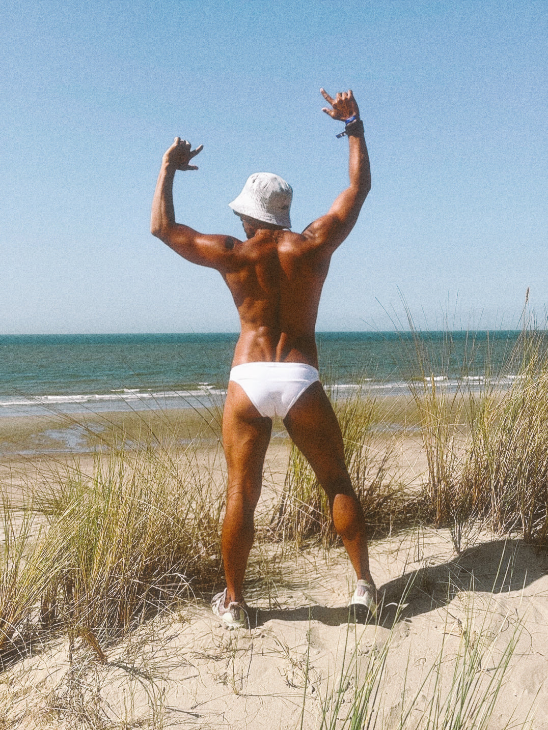 Latino in white underwear standing on a beach with ocean view